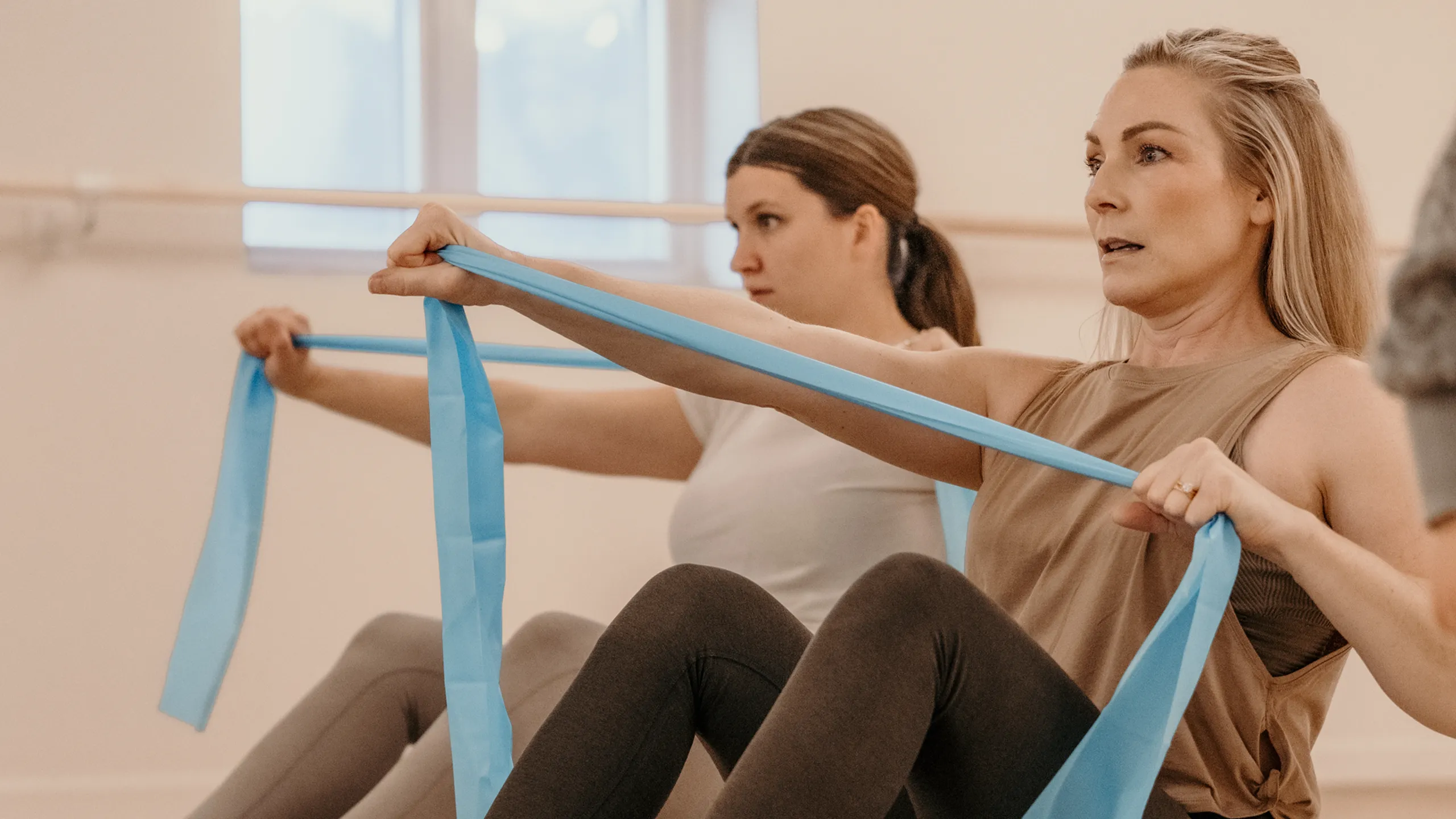 Two women seated and pulling resistance bands during a group fitness class at Breathe Studio in Pequot Lakes, MN.