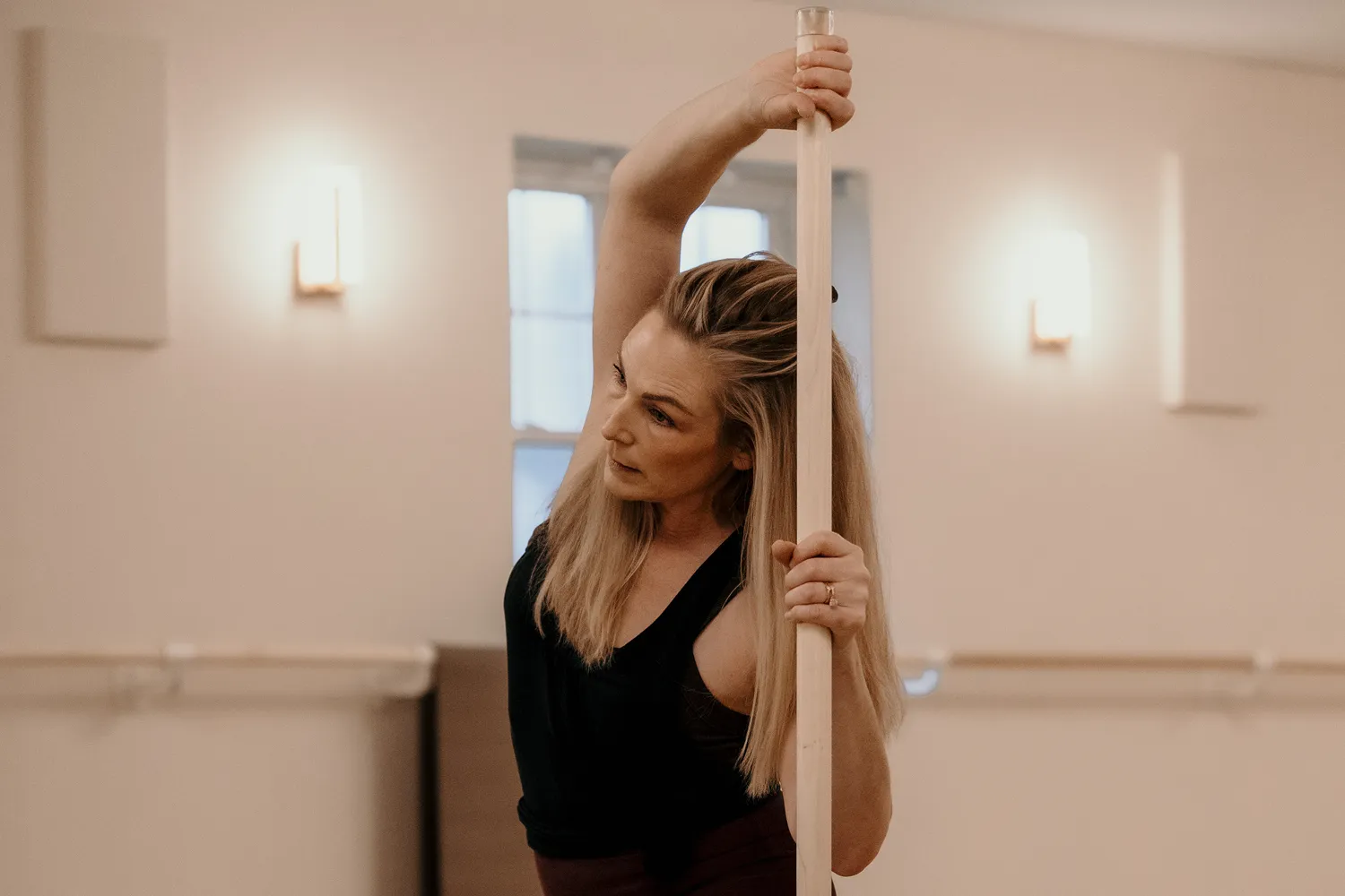 Woman performing a side-body mobility stretch using a dowel in Mobility Method class.