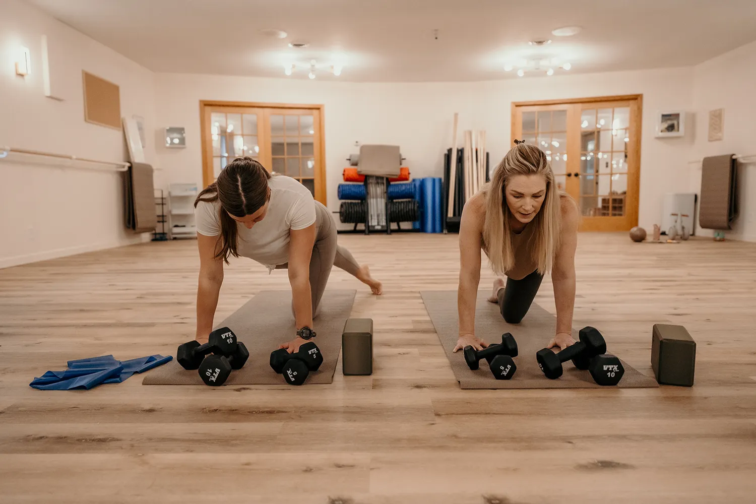 Personal trainer guiding a female client through a plank exercise with dumbbells during a private training session.