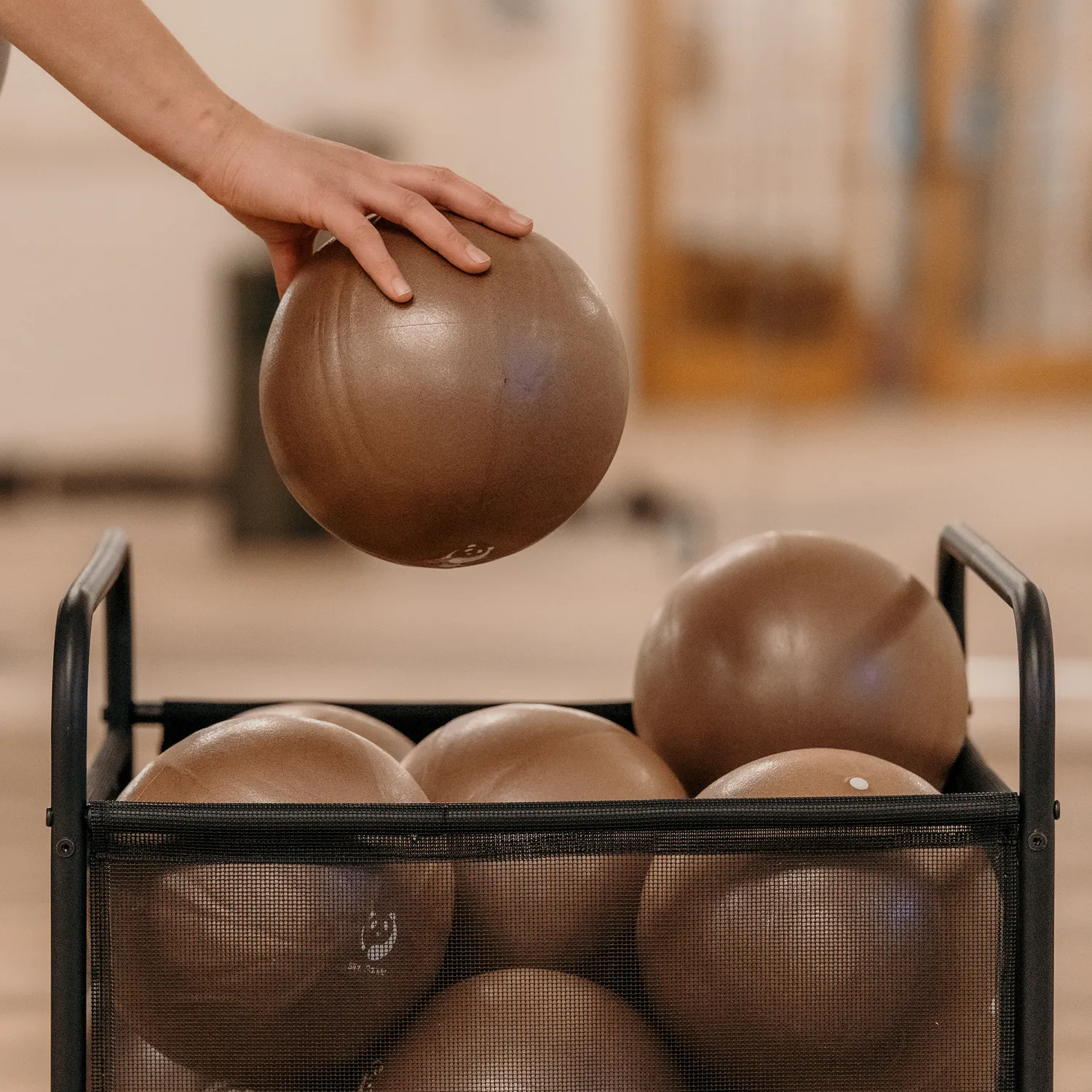 Hand reaching for a small exercise ball from a storage cart in the fitness studio.