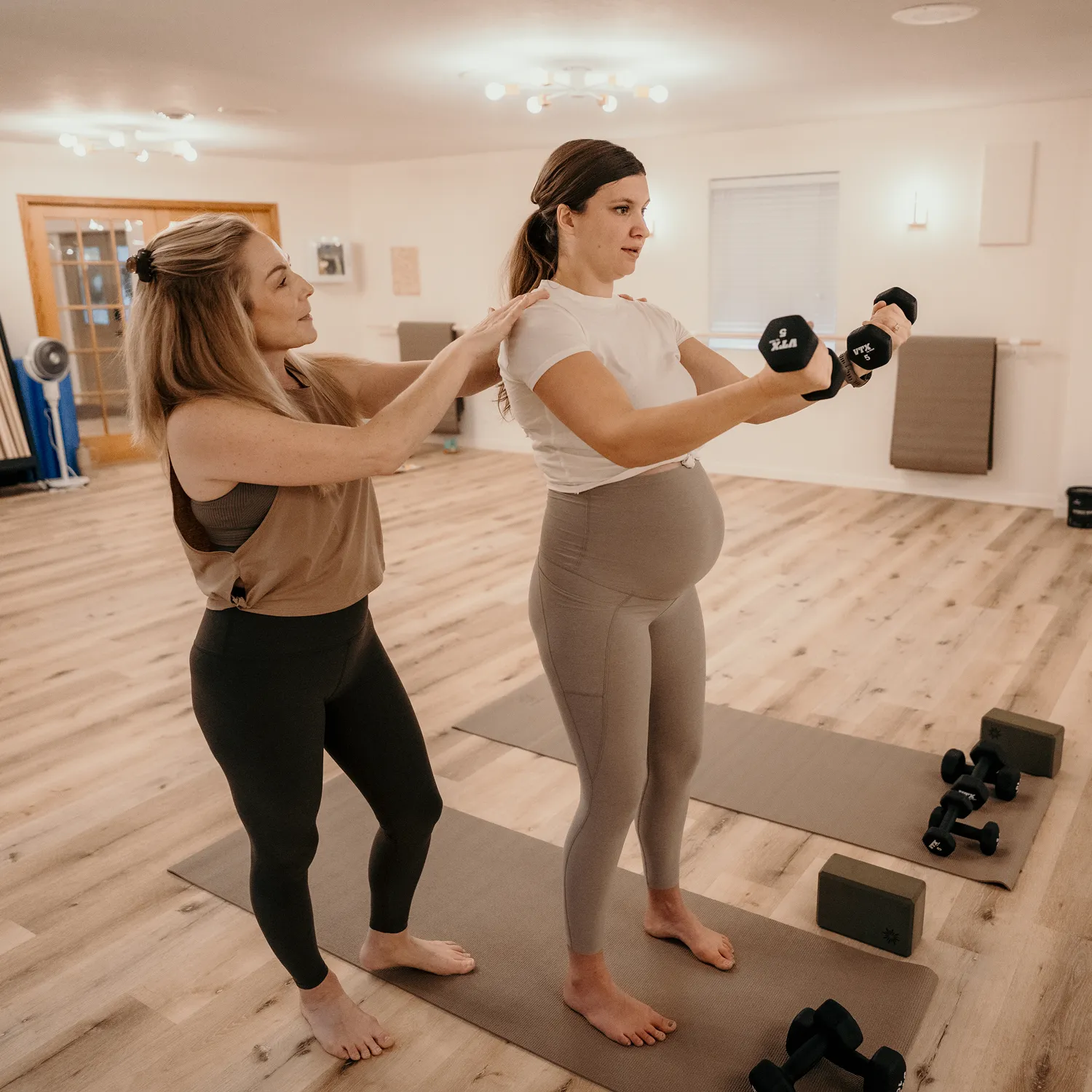 Personal trainer supporting a pregnant woman during a strength training session with dumbbells.